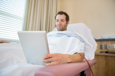 Happy young male patient using tablet computer during renal dialysis treatment in hospital room